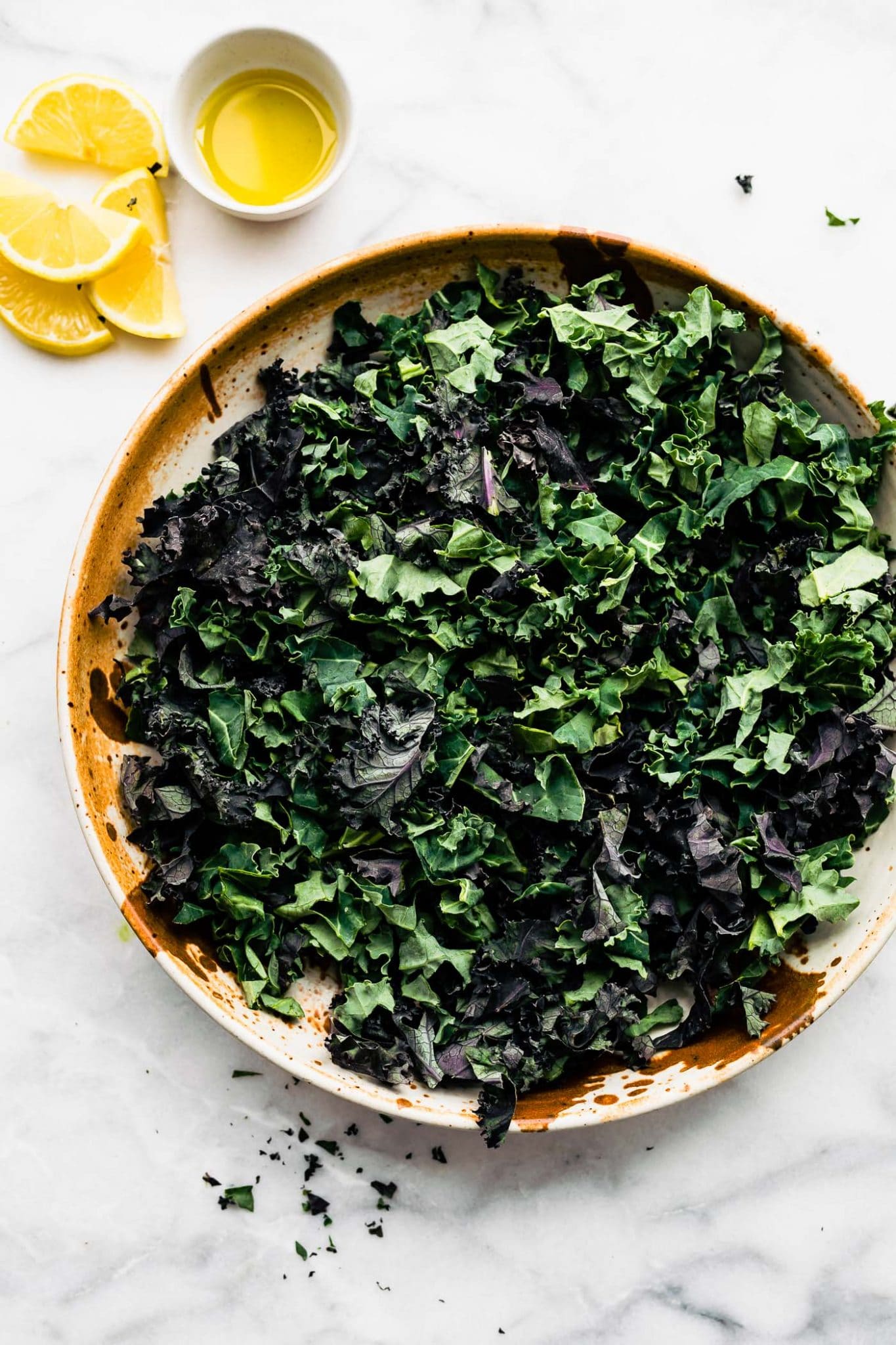 overhead image of purple and green kale in tan bowl with oil and lemon on the side
