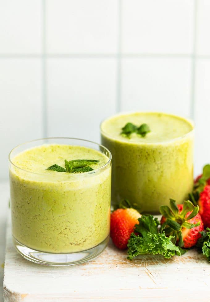 Two berry and kale smoothies prepared with fresh mint leaves, surrounded by strawberries