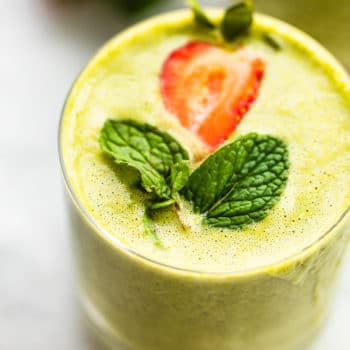 Image of a glass filled with blended super fruit kale smoothie, topped with fresh mint and strawberry