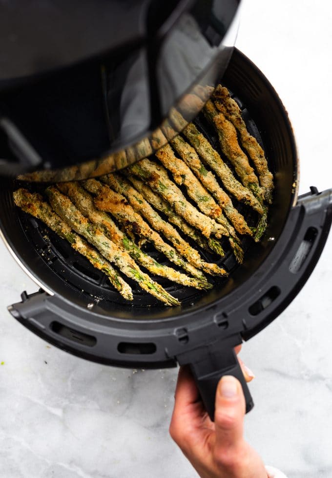 A hand pulling an air fryer basket out lined up with asparagus fries
