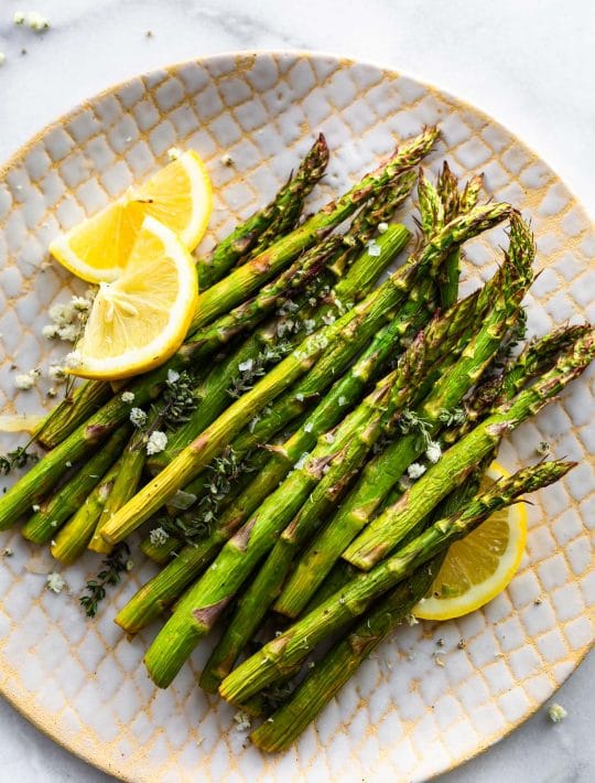 Overhead image of air fryer roasted asparagus on a plate with thin wedges of lemon.