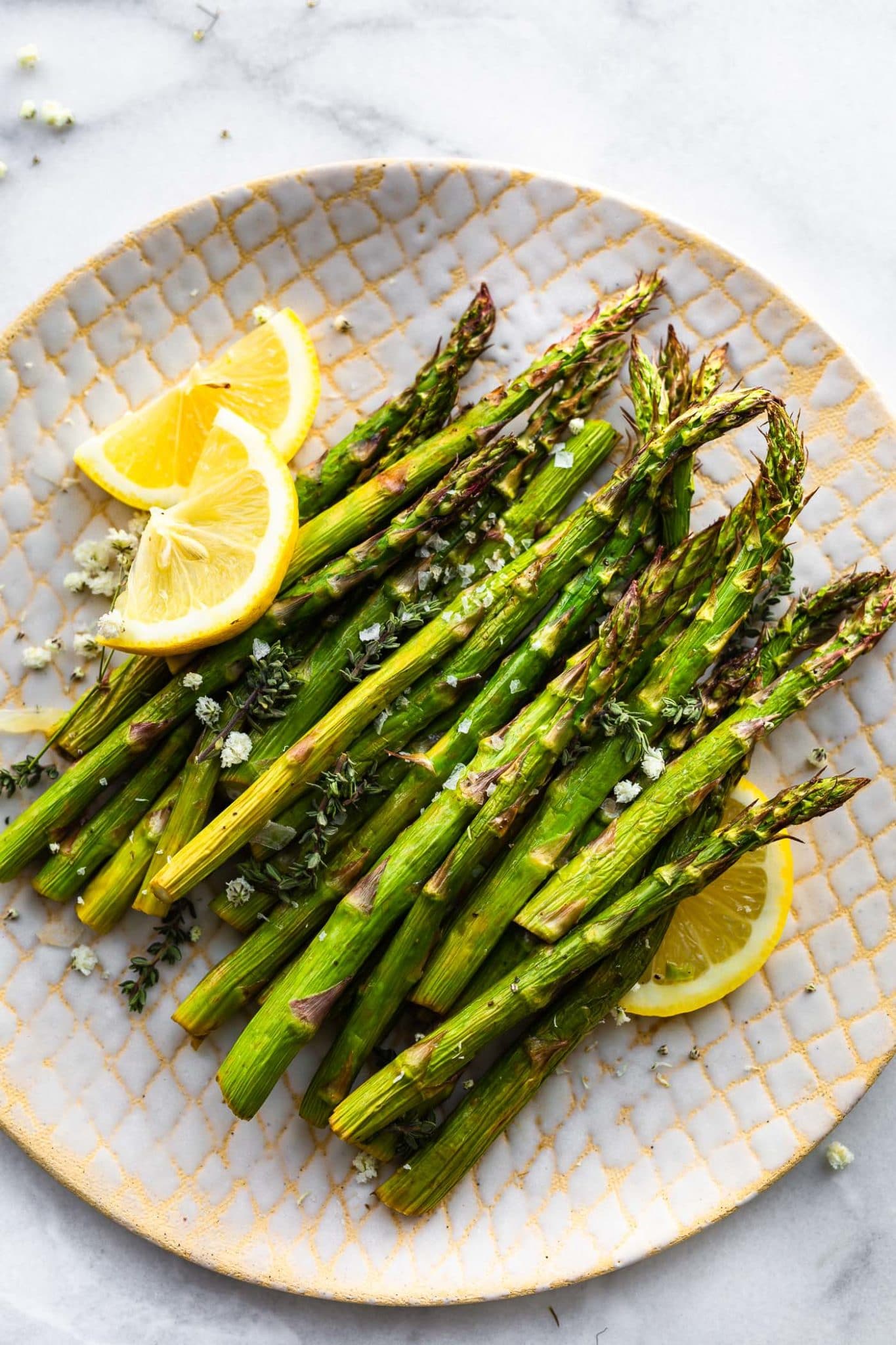 Overhead image of air fryer roasted asparagus on a plate with thin wedges of lemon.