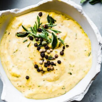 Overhead photo of garlic aioli with peppercorns and herbs in a white bowl.