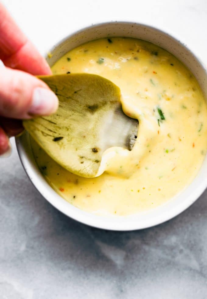 An instant pot steamed artichoke leaf being dipped into aioli sauce in a white bowl.