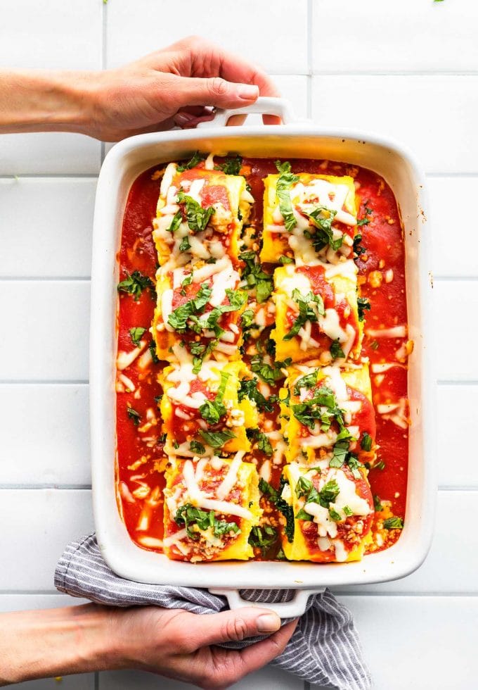 Overhead image of prepared keto egg lasagna roll ups in casserole dish covered in tomato sauce, cheese, and herbs