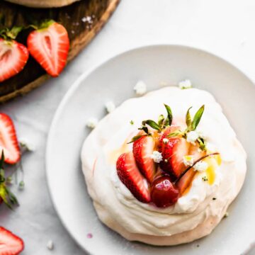 Overhead image of strawberry topped pavlova on a marble table with strawberries on the side.