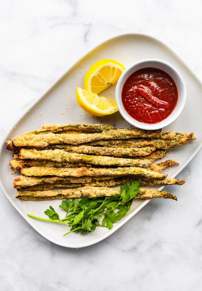 a serving platter of Air Fryer Asparagus Fries with ketchup and lemon wedges on the side