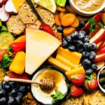 Overhead image of snack board with crackers, cheese, fresh produce, and homemade dips.