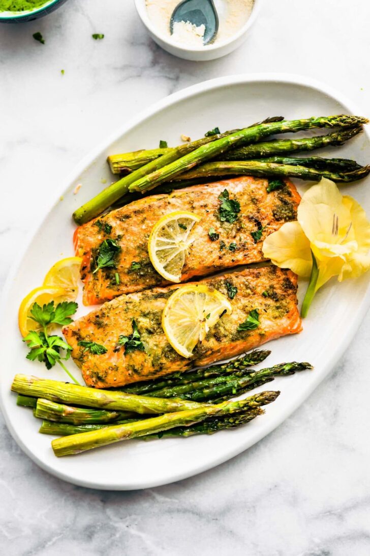 Baked salmon filets surrounded by roasted asparagus and topped with lemon slices and parsley