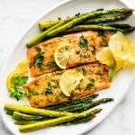 overhead photo of salmon on baking white placec with asparagus on the side