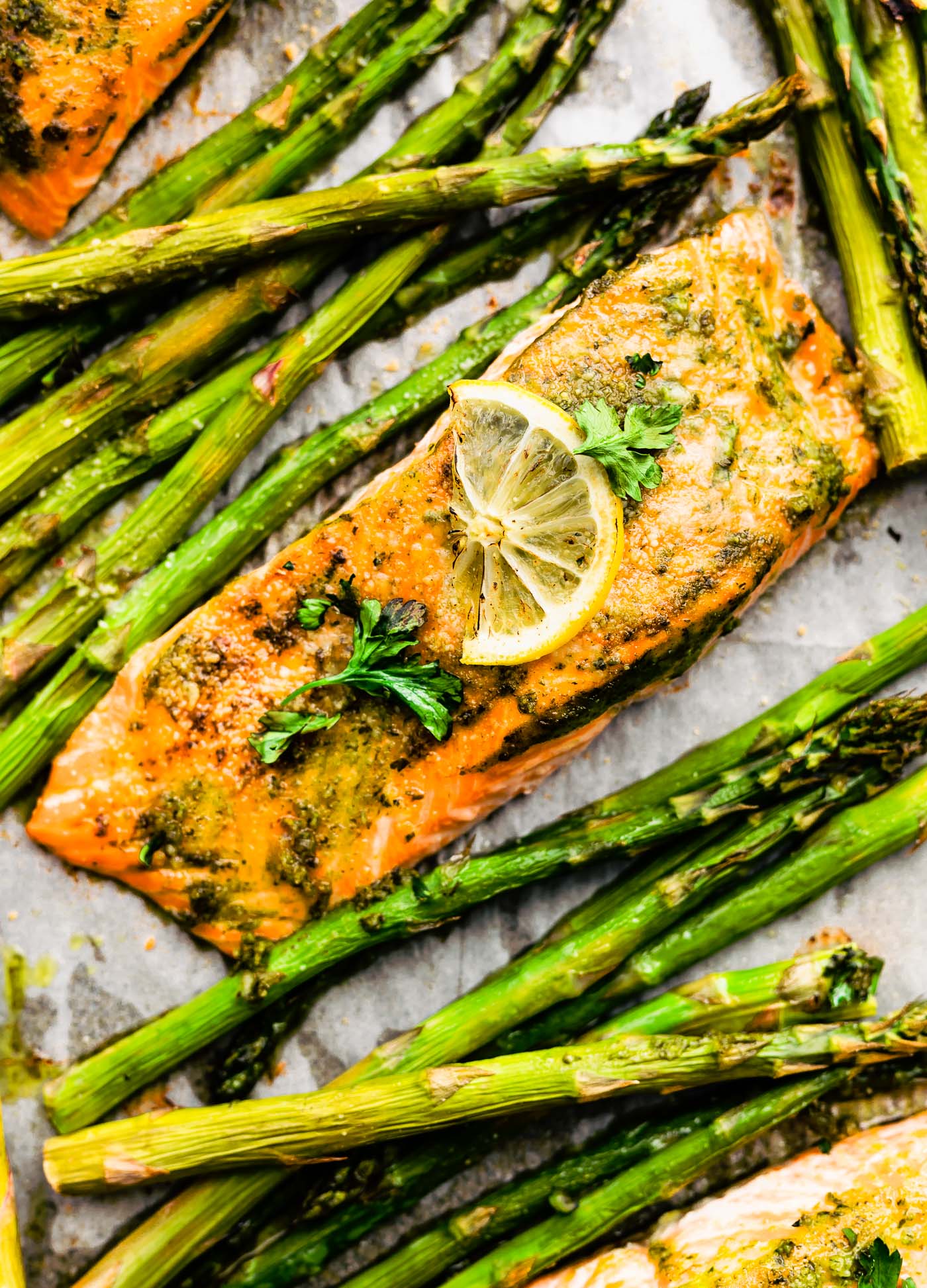 Close up overhead view of herb crusted baked salmon and roasted asparagus spears on parchment-lined baking sheet.