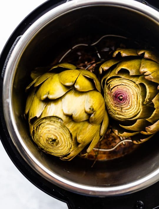 overhead photos of cooked artichokes in an instant pot. Pressure cooked artichokes with lid off the pot