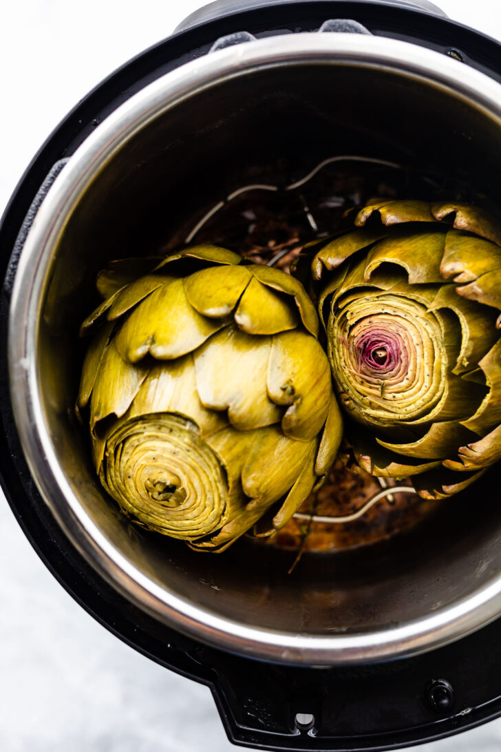 Overhead photos of cooked artichokes in an instant pot. Pressure cooked artichokes with lid off the pot.
