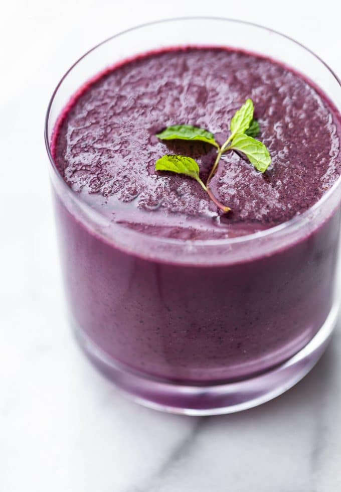 Image of a glass filled with blended berries and kale smoothie, topped with fresh mint