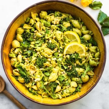 Green goddess pasta salad on a tabletop with yellow flowers and a wooden spoon.