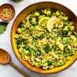 Overhead image of vegan green goddess pasta salad with a wooden spoon and flowers.