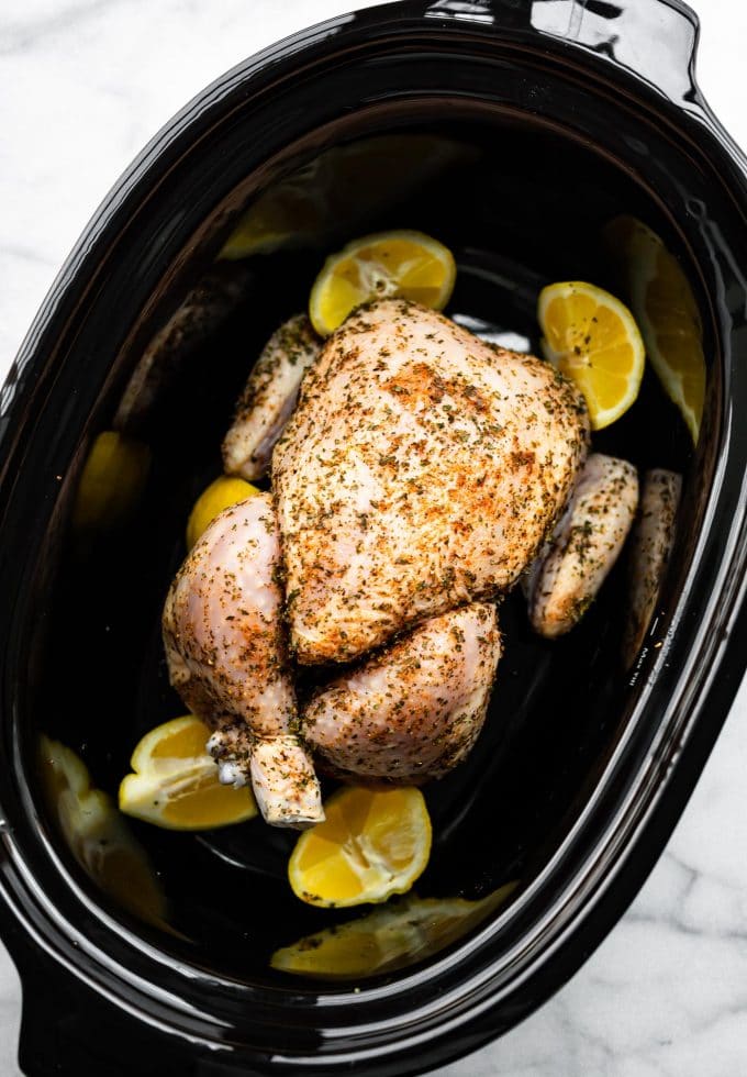 Overhead view whole chicken in black slow cooker with lemons.