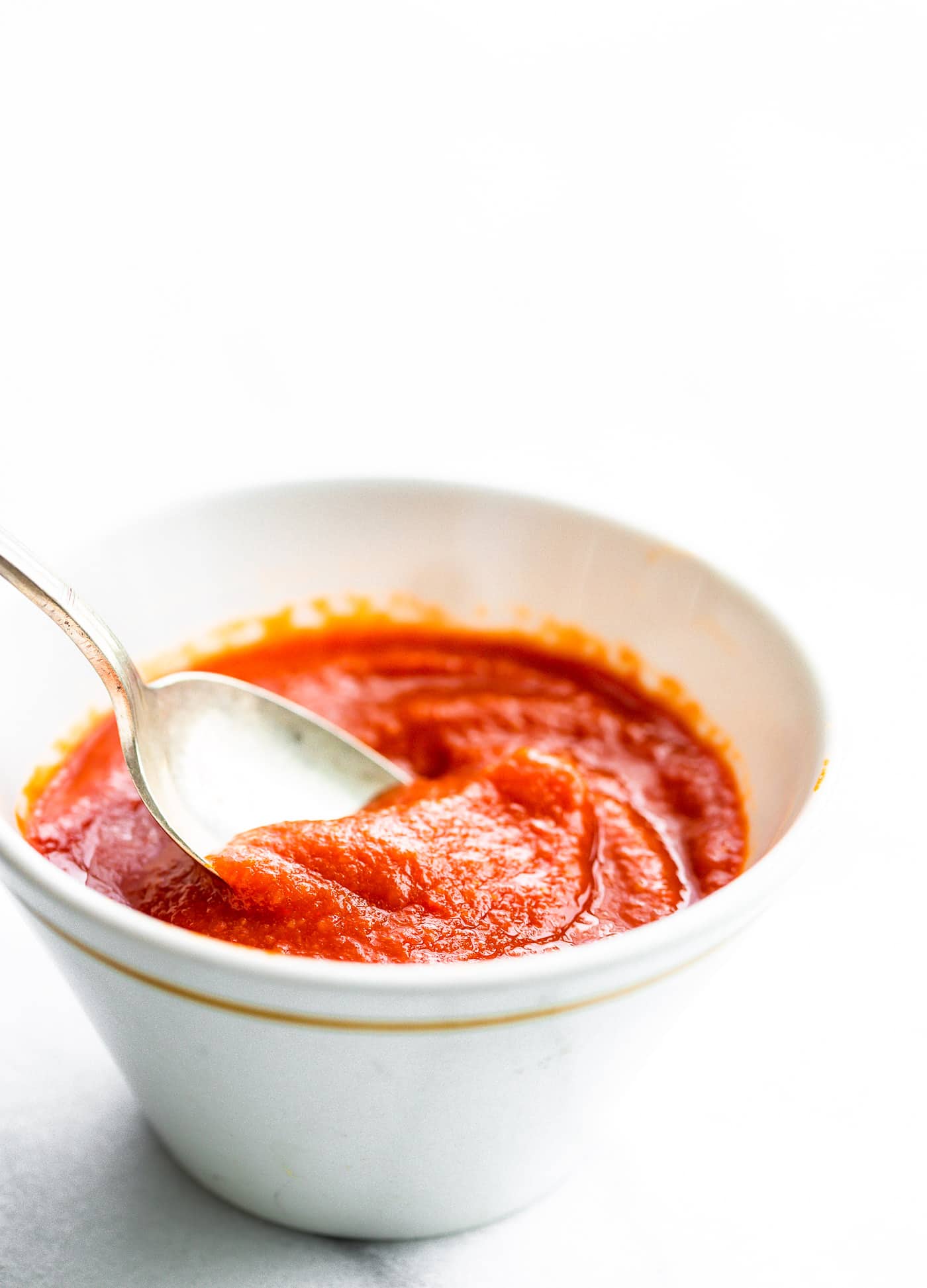 Close up image of homemade hot sauce in a white bowl with a silver spoon.