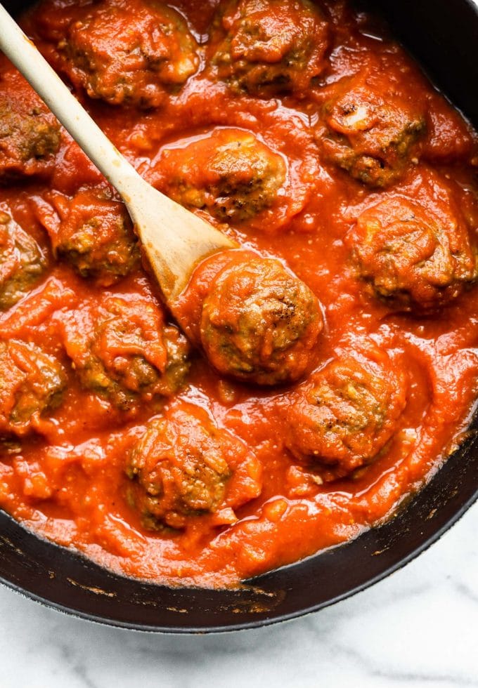 Overhead image of meatballs in a skillet with homemade sauce and a wooden spoon.