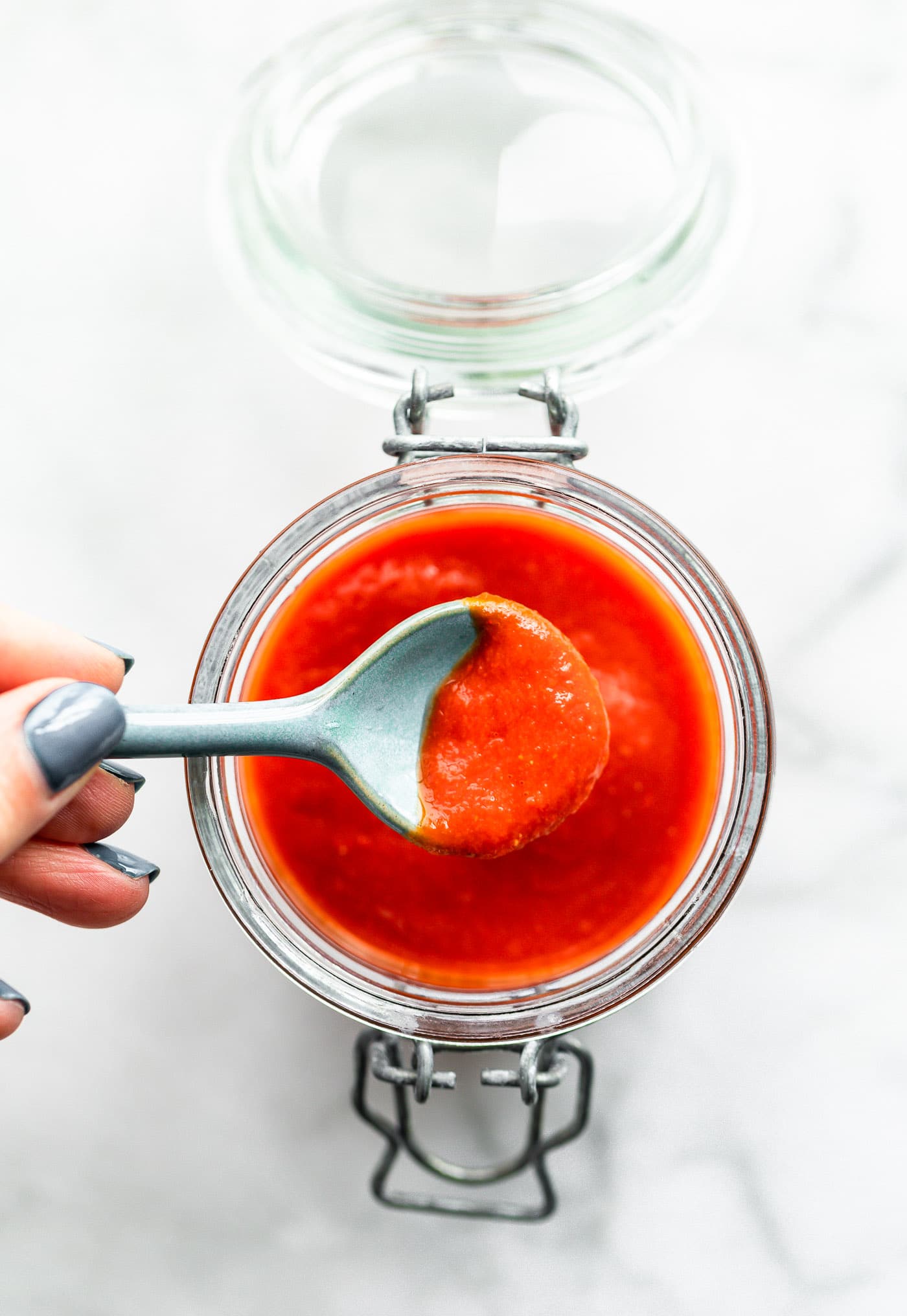 Overhead image of a spoonful of homemade sriracha sauce being lifted out of a storage jar.