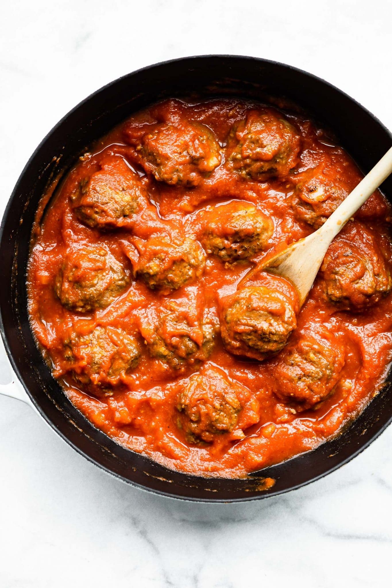 Overhead image of a skillet with meatballs and sauce with a wooden spoon.