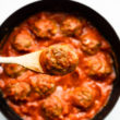 Overhead image of a spoon lifting a turkey meatball from a skillet with sauce.