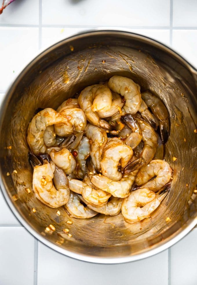Overhead view silver bowl filled with raw shrimp marinating in chile-ginger marinade.