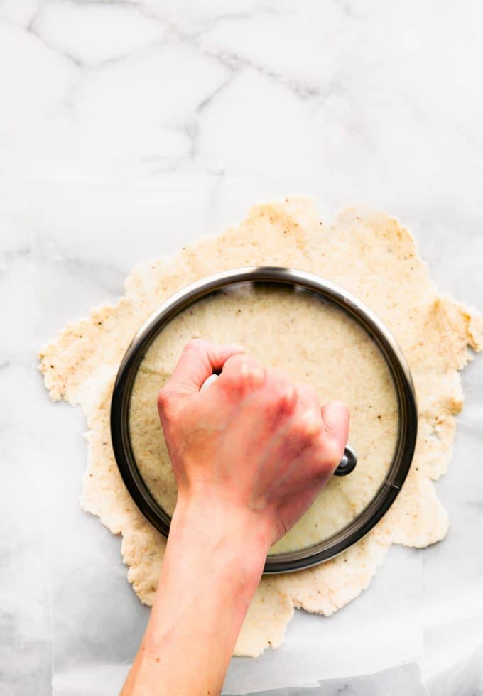 A hand pressing a saucepan lid into center of rolled out coconut flour tortilla dough.