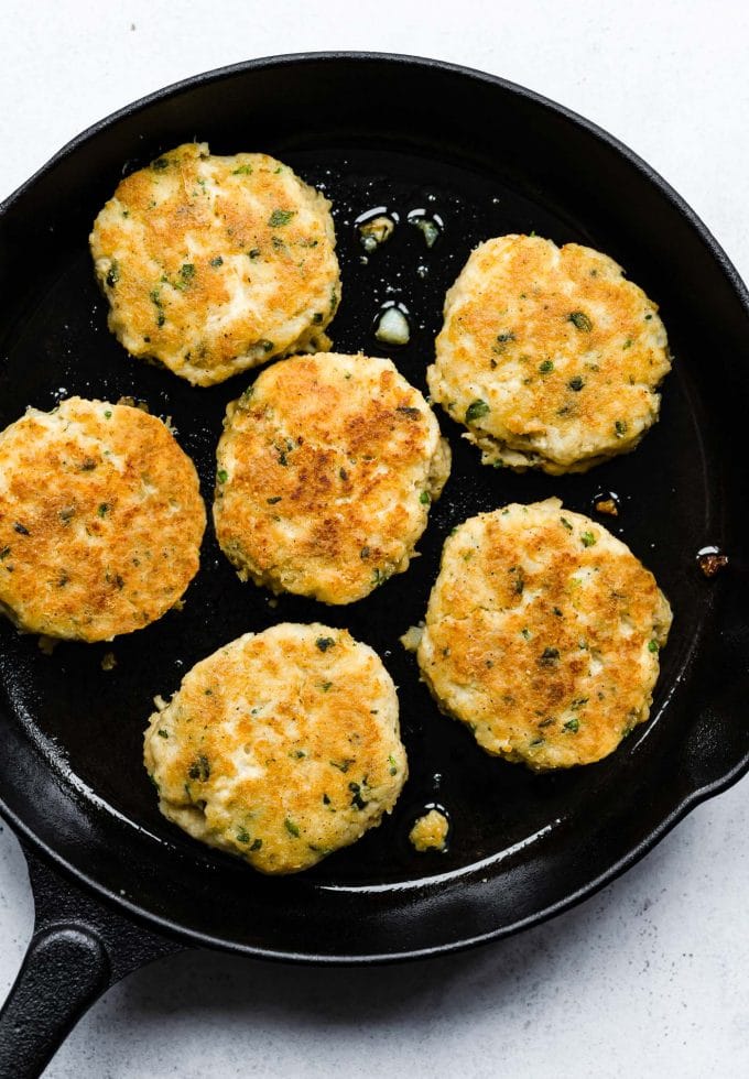 Several cod cakes cooking in a cast iron skillet