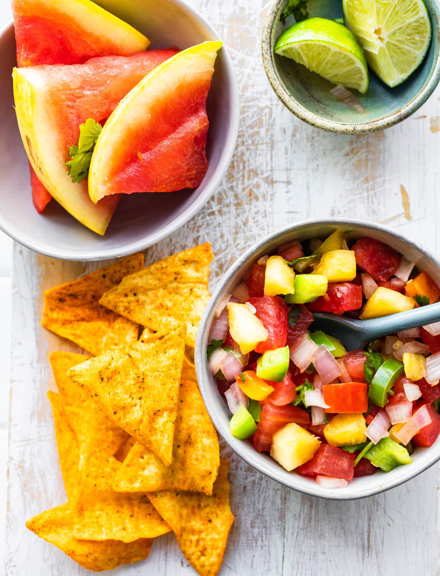 overhead image of watermelon pineapple salsa next to chips, limes, and more watermelon