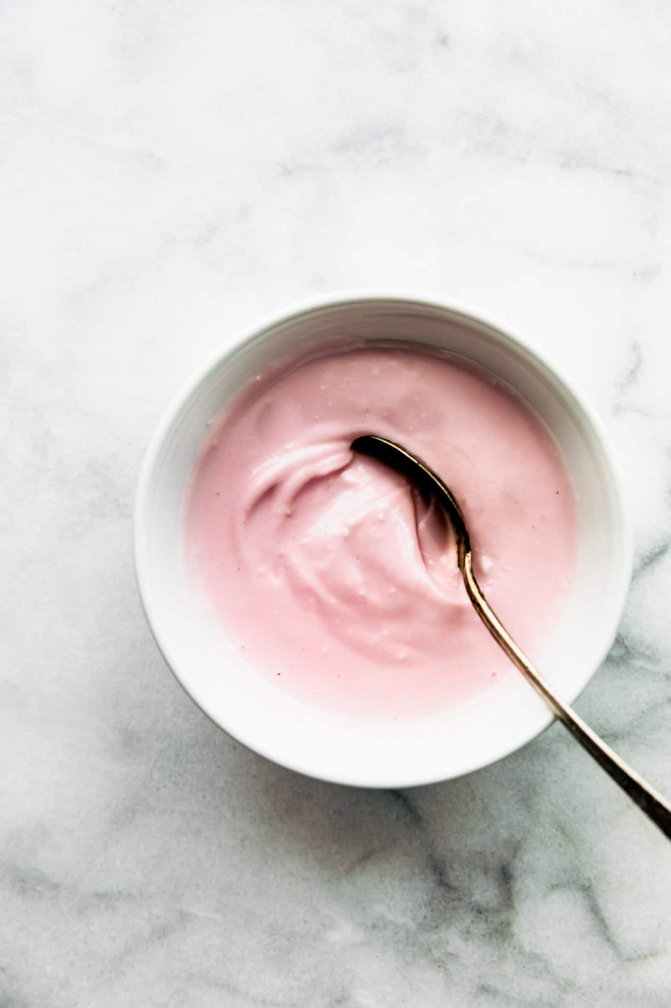 Overhead view pink Greek yogurt frosting in white bowl with spoon.