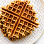 Overhead photo of a stack of peanut butter waffles on a white textured plate.