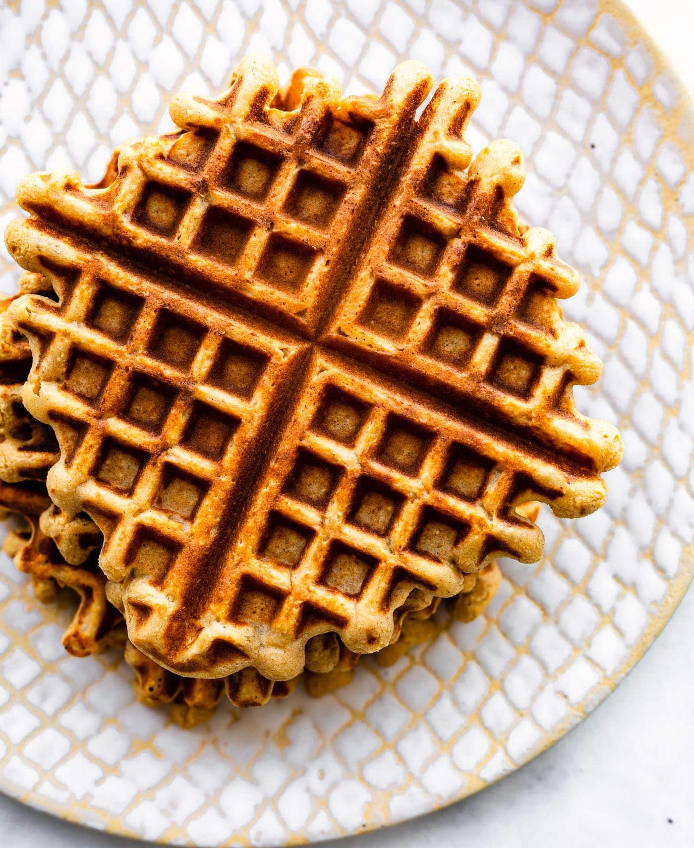 Overhead photo of a stack of peanut butter waffles on a white textured plate.