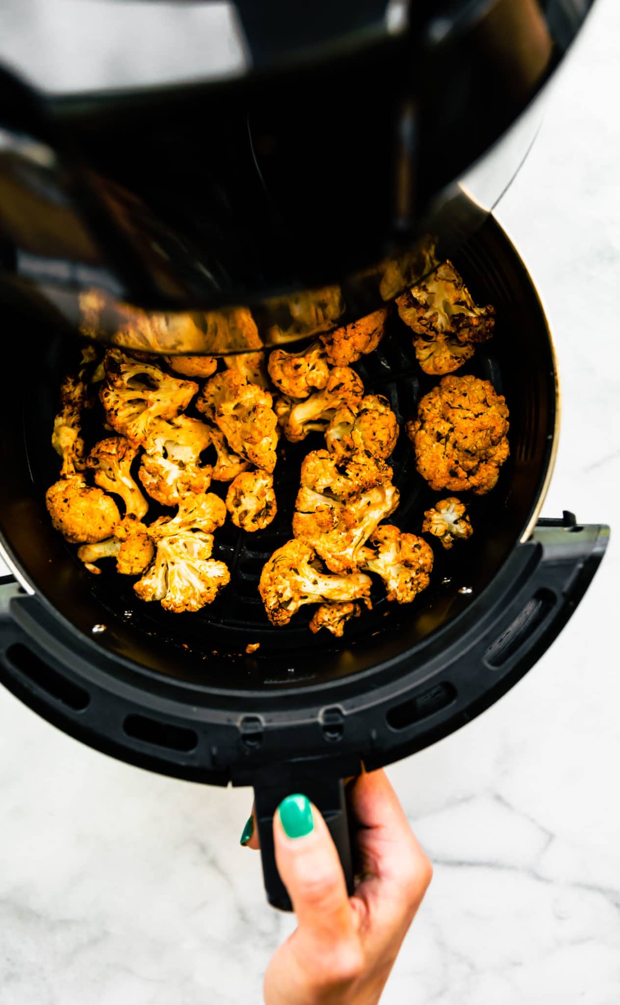 air fryer cauliflower florets being pulled out of an air fryer