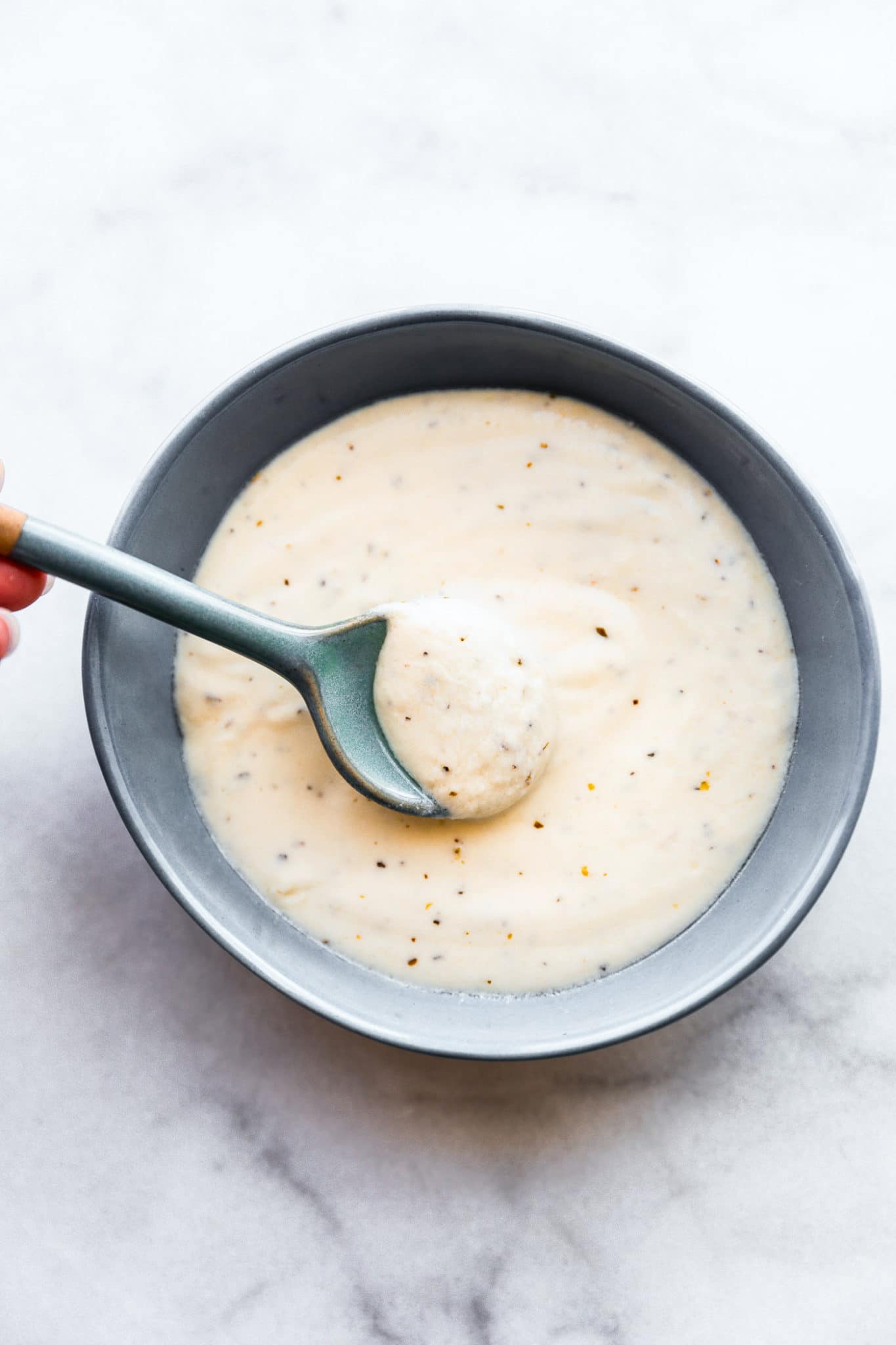 Homemade alfredo sauce in a gray bowl being dipped with a gray spoon