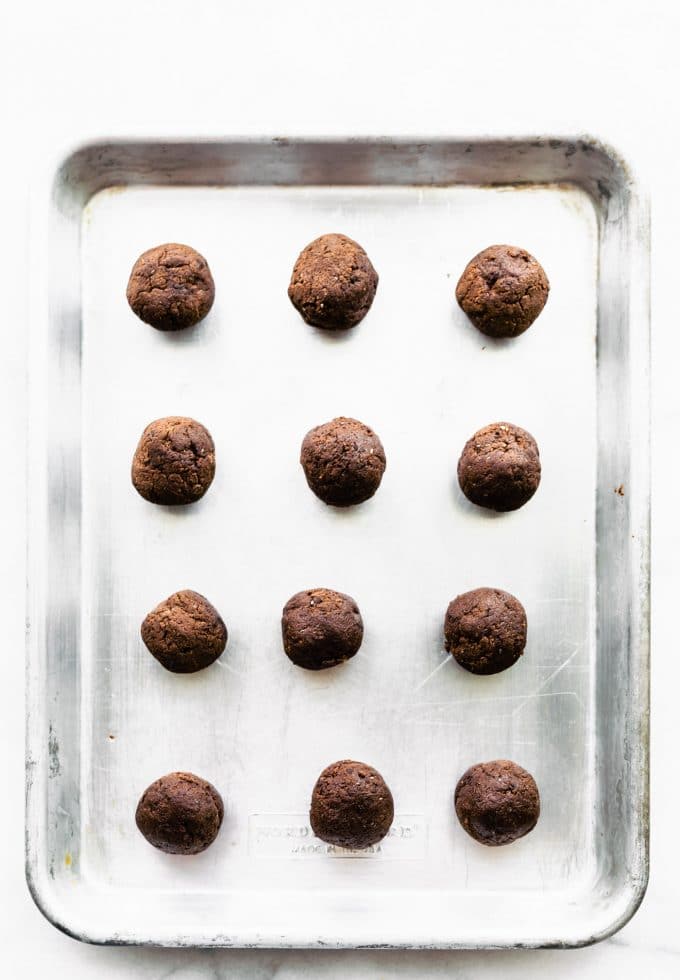 Vegan chocolate protein cookie dough balls lined up on silver baking sheet.