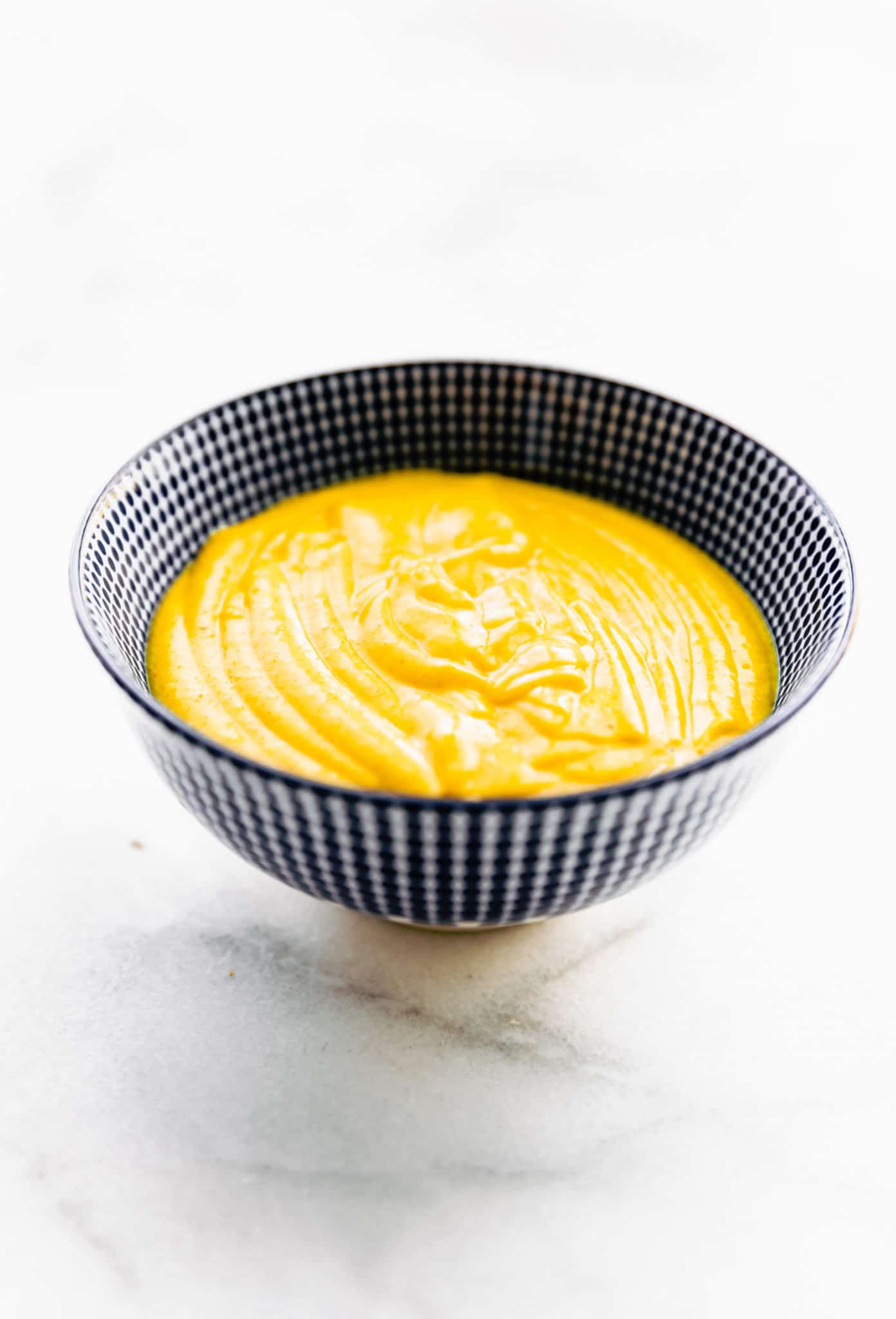 Vegan cheese sauce in a blue bowl on a white tabletop