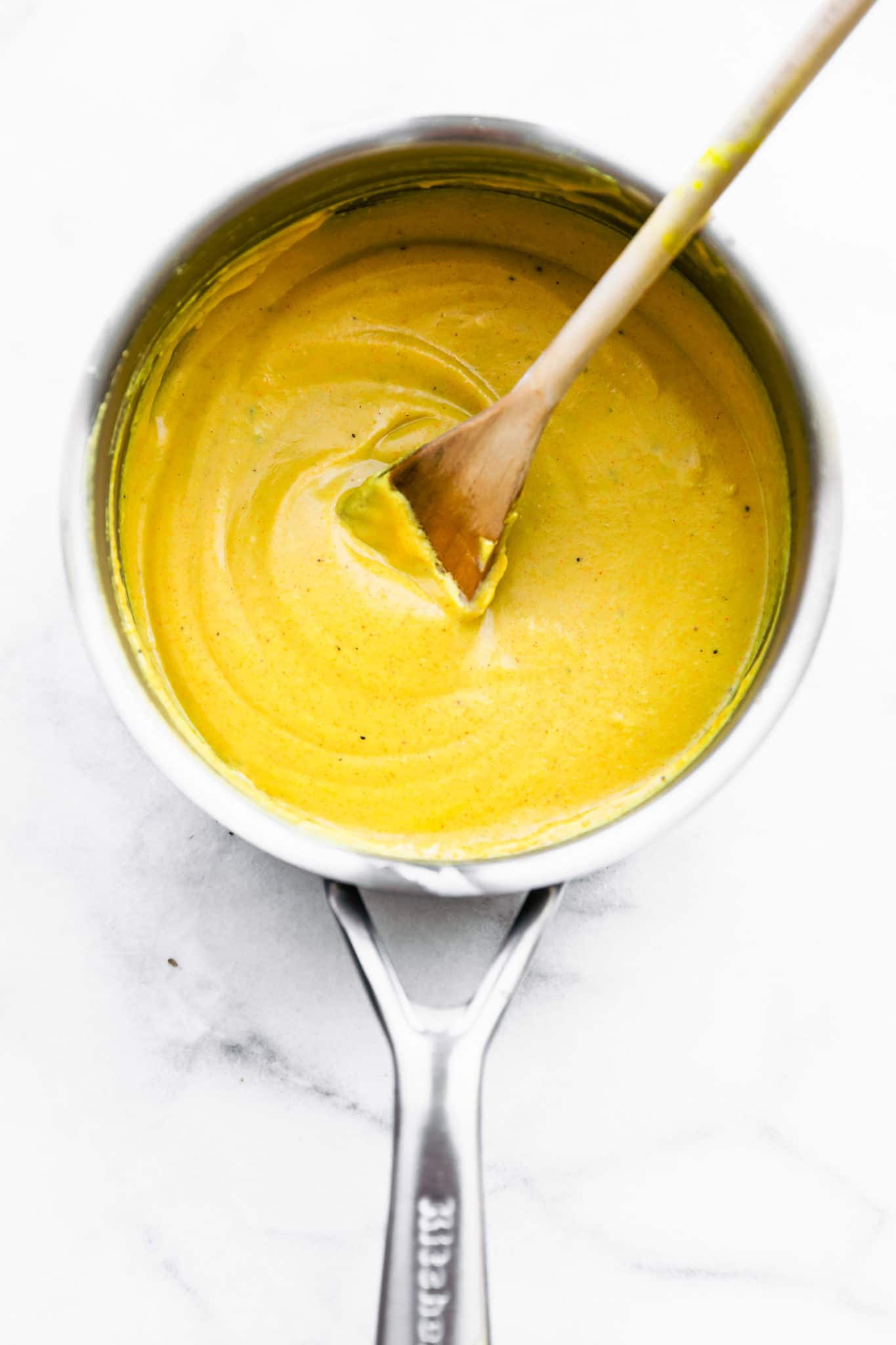Overhead image of vegan cheese sauce using nutritional yeast with a wooden spoon.