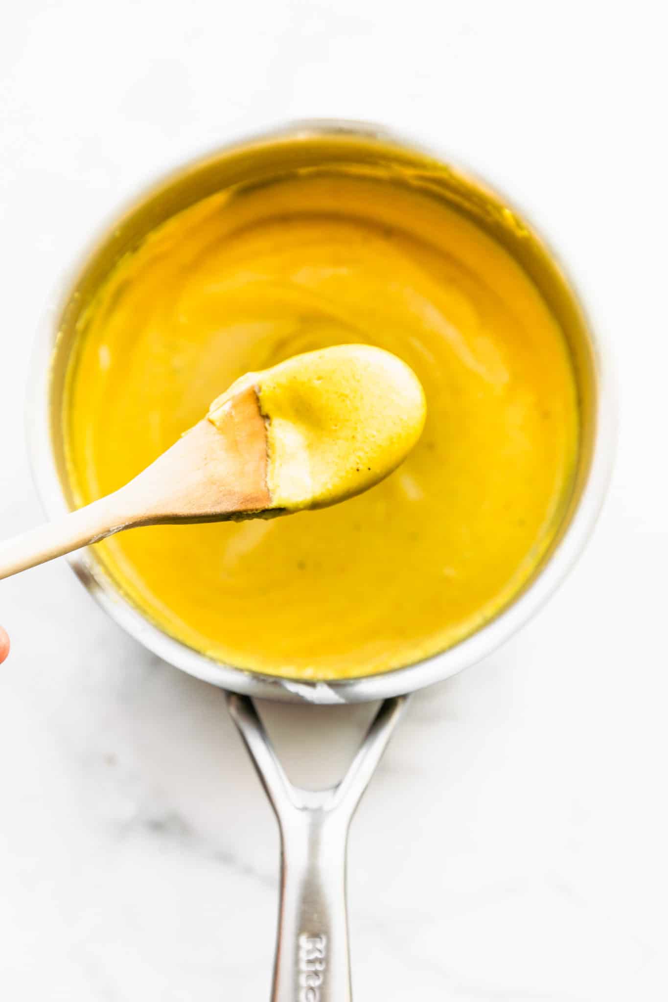overhead image of a spoon of vegan cheese sauce for mac and cheese being held over a pot.