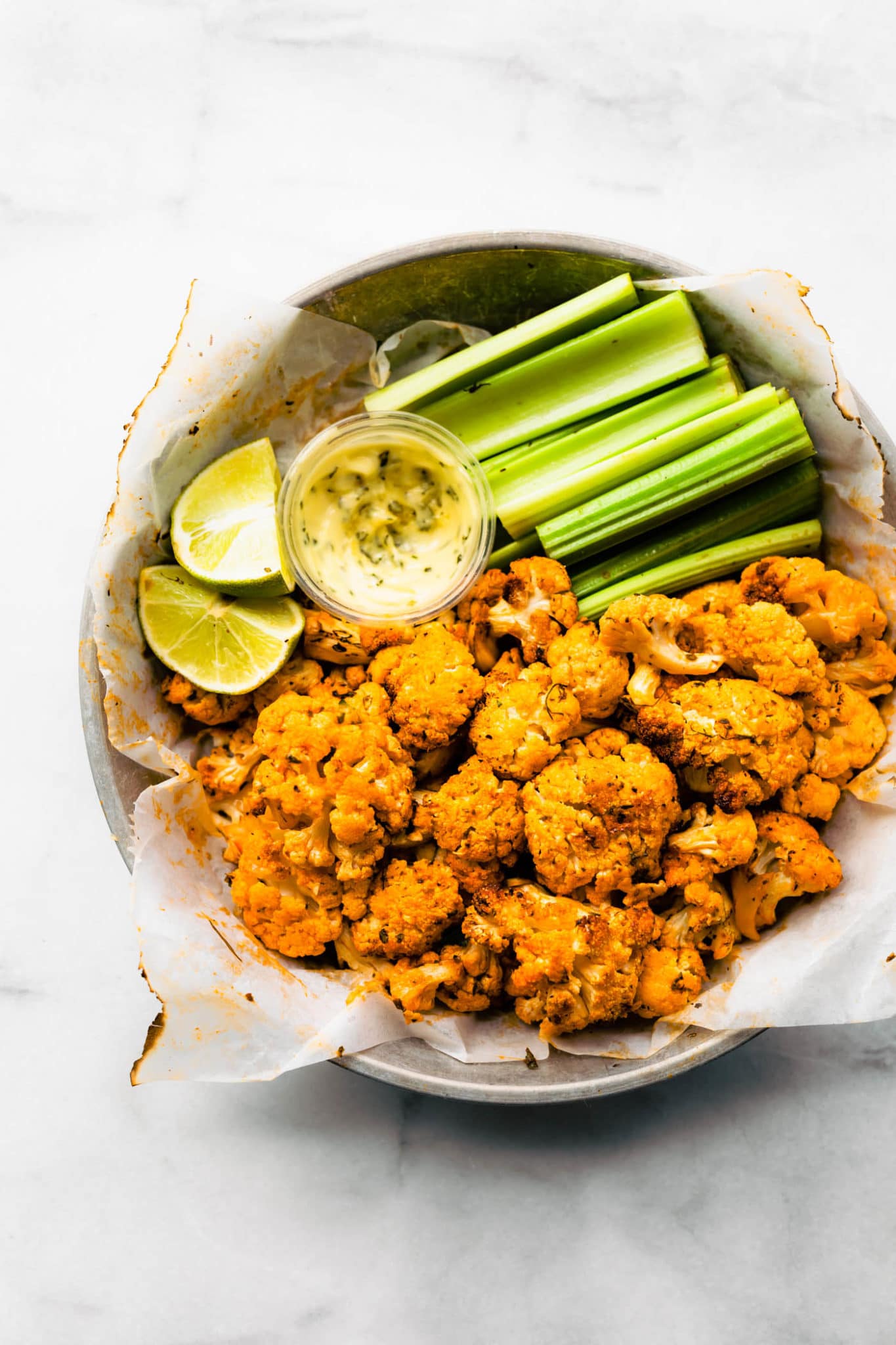 overhead shot of air fried buffalo cauliflower in tin plate with celery and dipping sauce