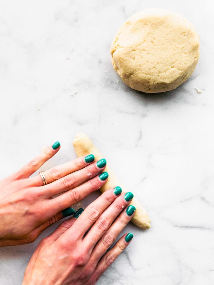 Two hands rolling cauliflower gnocchi dough on marble countertop.