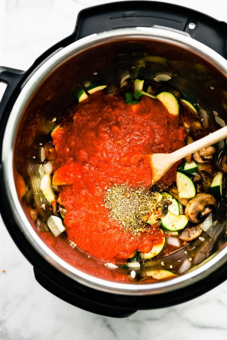 tomato sauce and seasonings beign poured on top of mushrooms, onions, and zucchini in an instant pot