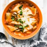 Instant pot lasagna noodle soup with veggies topped with cheese and fresh herbs served in a bowl with a spoon and a blue and white striped towel