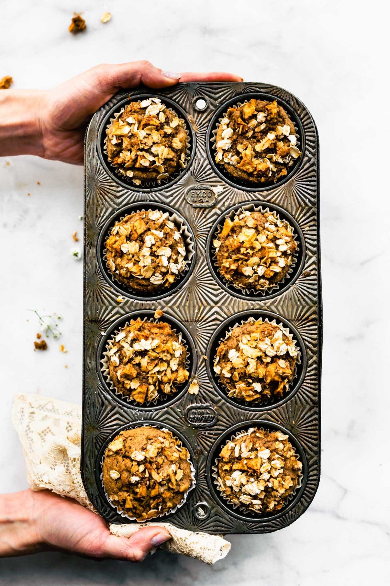 muffin tin with gluten free apple oatmeal muffin being held wtih 2 hands