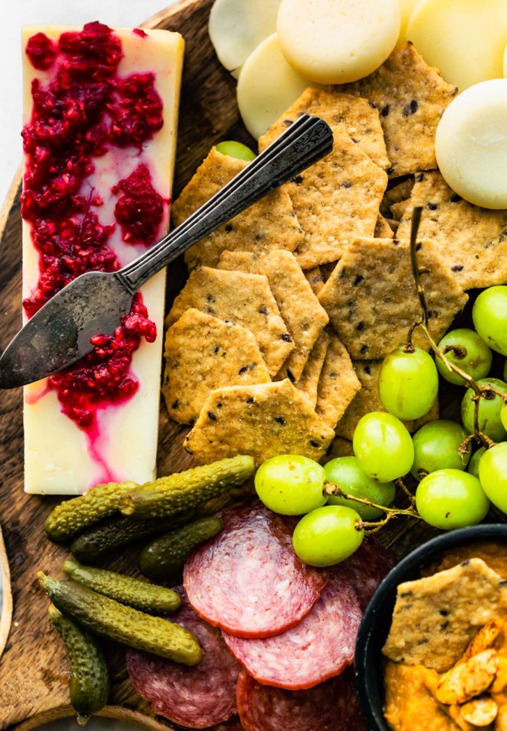 Close up overhead view charcuterie board with crackers, grapes, salami, and hard cheese.