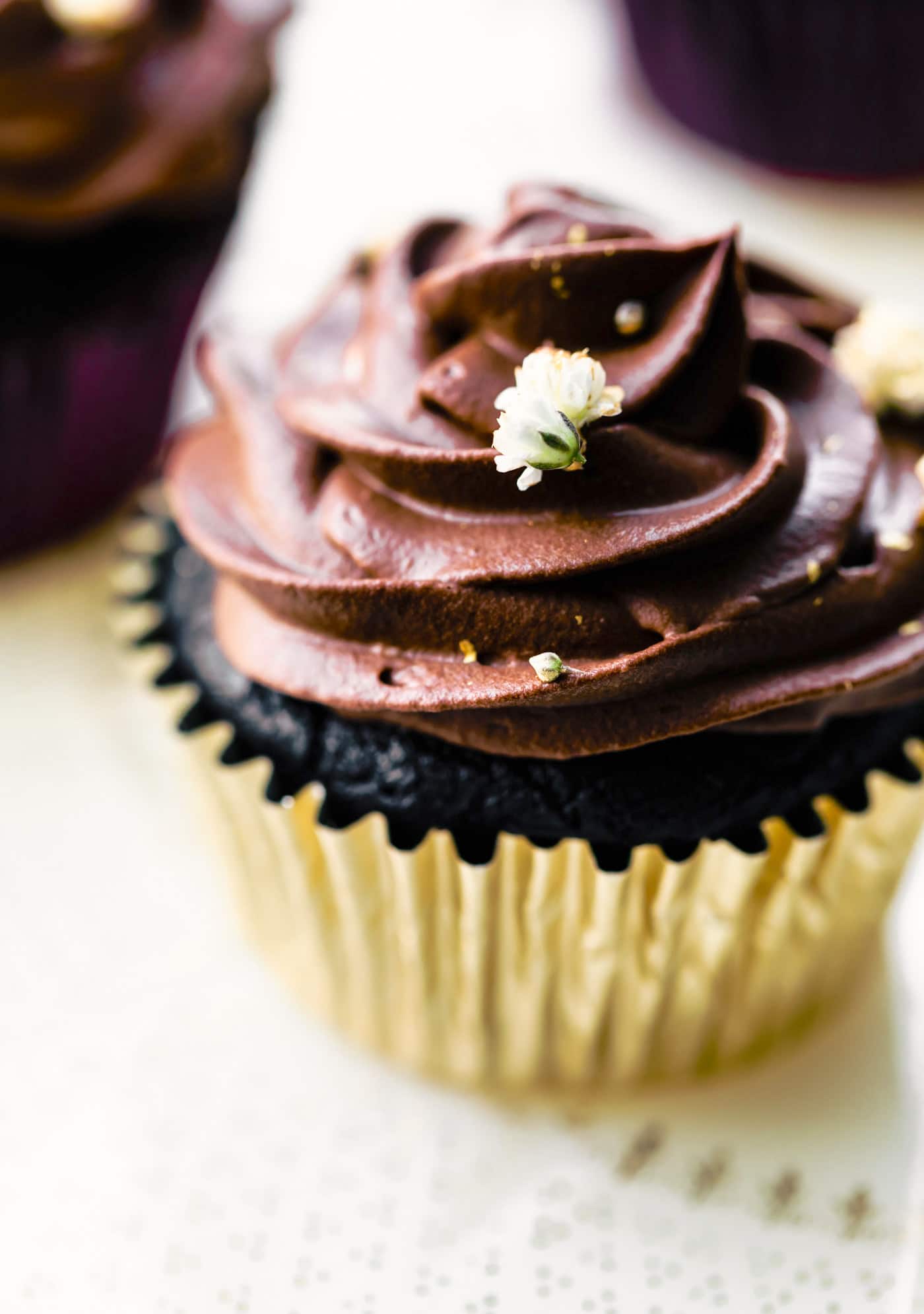 Up close photo of a chocolate cupcake topped with chocolate frosting and a white flower.