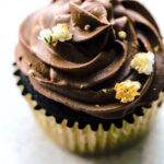 Up close overhead photo of a chocolate cupcake topped with chocolate frosting and flowers.