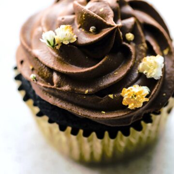 Up close overhead photo of a chocolate cupcake topped with chocolate frosting and flowers.