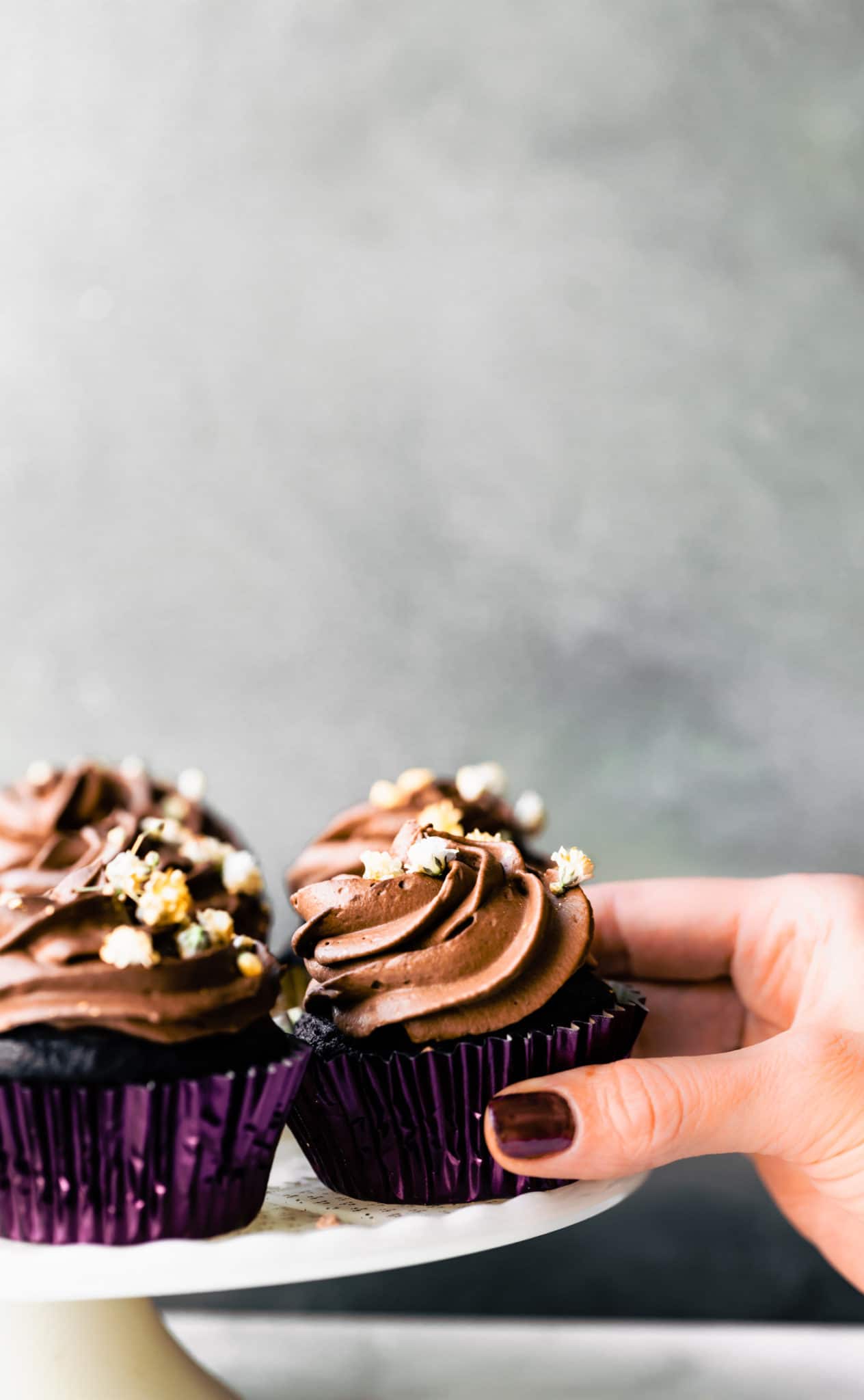 Hand grabbing an egg-free chocolate cupcake with chocolate frosting off a tray