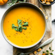 butternut squash soup surrounded by pumpkins, thyme, roasted pumpkin seeds, and a spoon